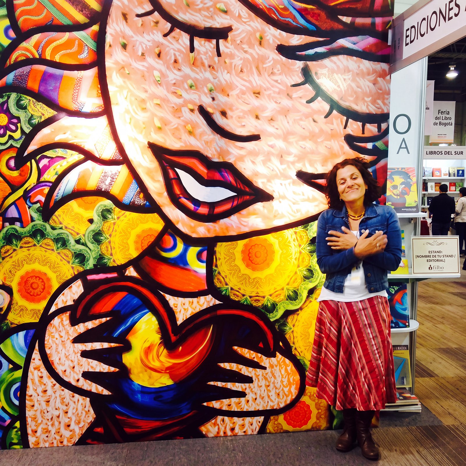 La fundadora de Colombia, un país con sentido, sonriendo con las manos en el pecho frente al mural ilustrado de su stand en la Feria del Libro de Bogotá