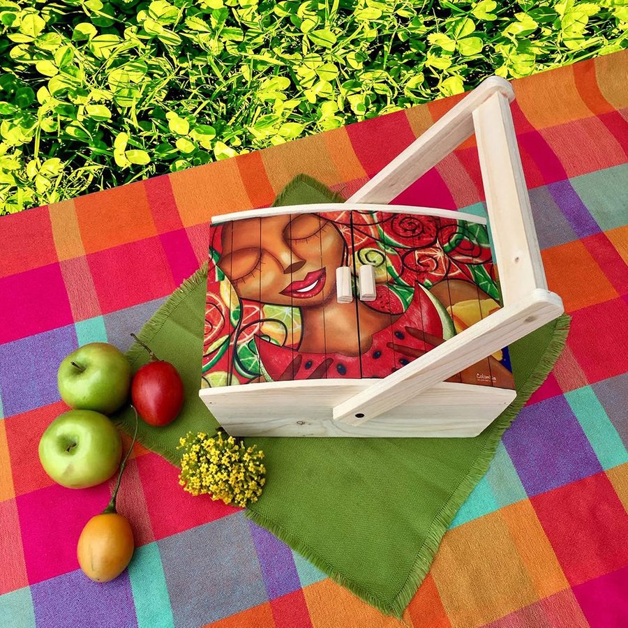 Canasta de picnic de madera con la tapa ilustrada, sobre un mantel de cuadros con frutas