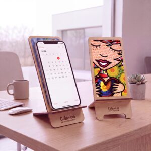 Dos soportes de madera para celular sobre un escritorio, uno con el teléfono puesto, con el logo grabado en la base